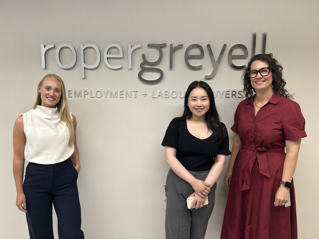 Roper Greyell's 2025-26 Articling Students. Pictured L-R: Larissa DeWolff, Tana Wang and Julia Brewster in front of Roper Greyell's lobby sign.